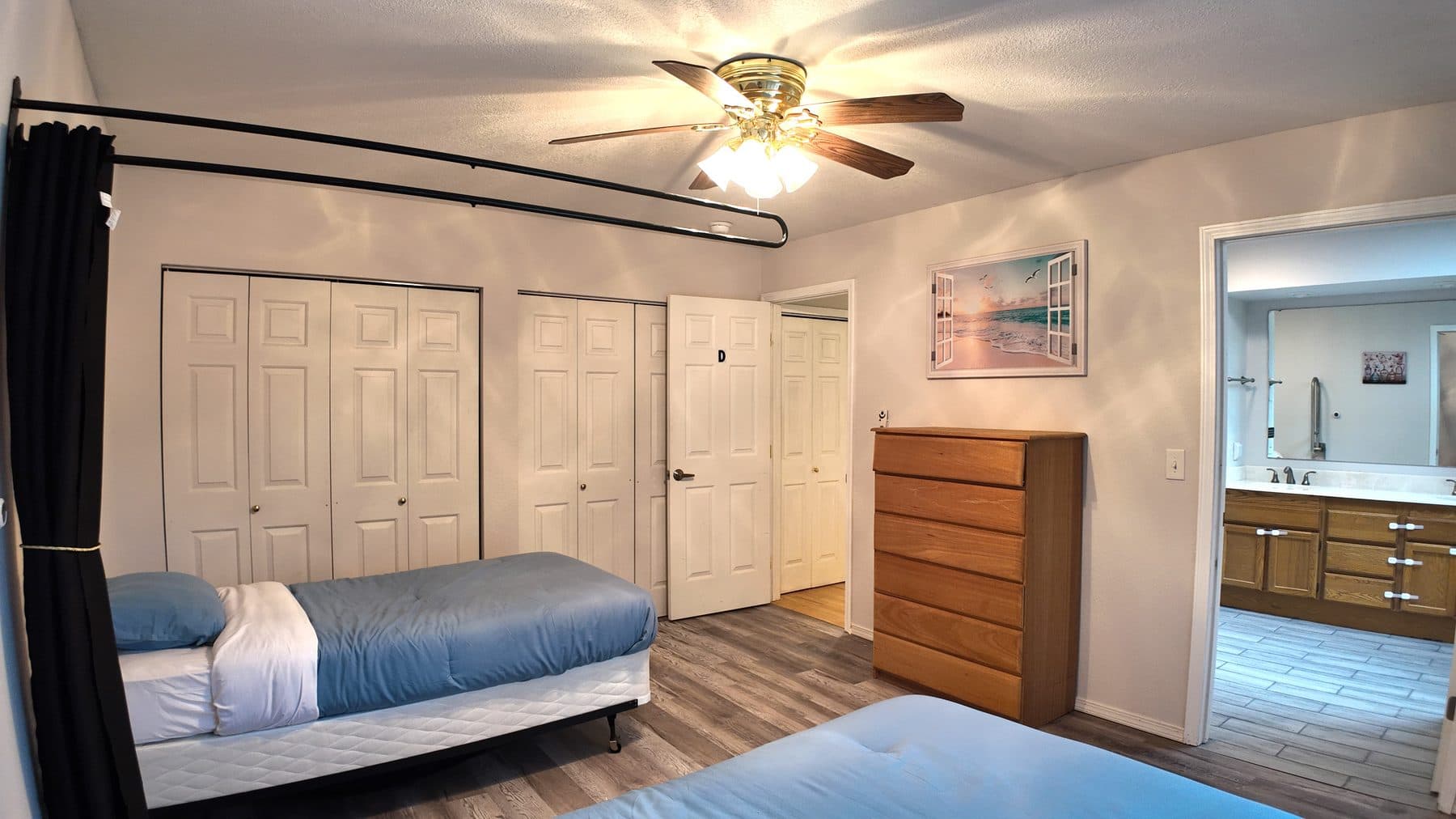Resident bedroom with a made bed, closets, a dresser and an adjoining bathroom