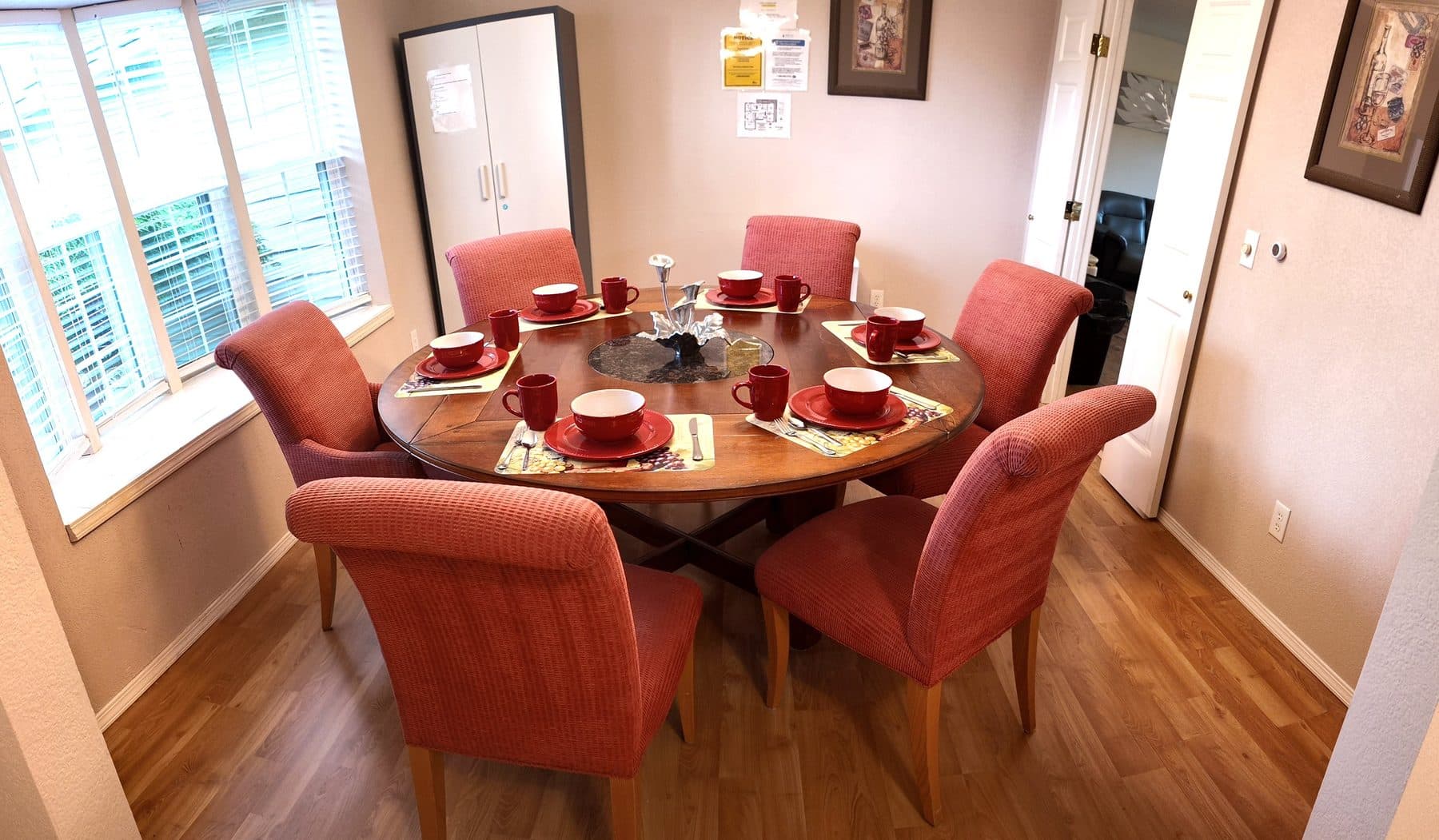 Dining room with a round table set for a meal, surrounded by cushioned chairs and windows